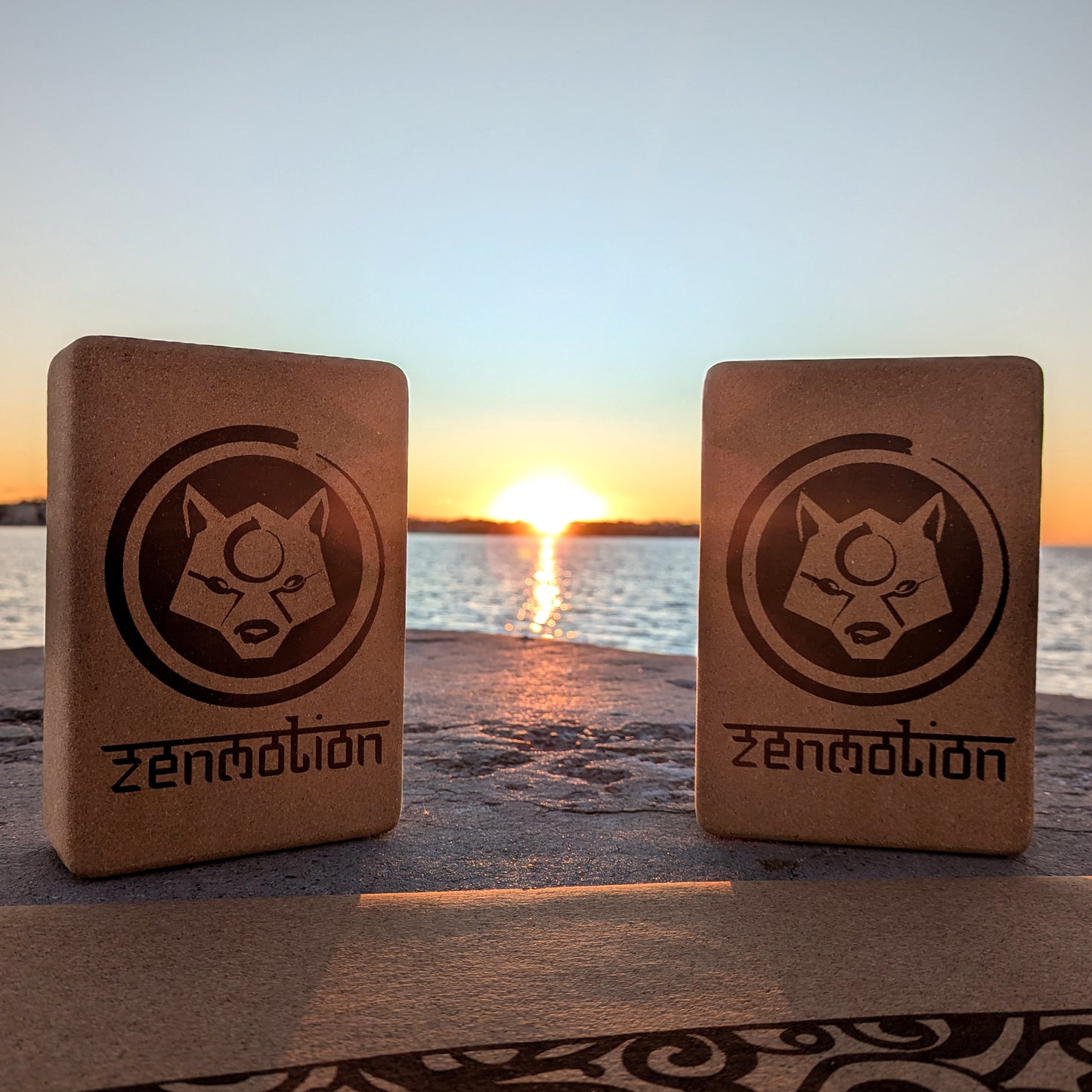 Deux briques de yoga ZenMotion posées sur un tapis en liège, avec un lever de soleil en bord de mer en arrière-plan. Accessoires écologiques et naturels, parfaits pour améliorer l'alignement, la souplesse et la stabilité lors de vos pratiques de Hatha, Vinyasa ou méditation. Une scène apaisante, symbolisant harmonie, énergie positive et connexion mindful avec la nature.