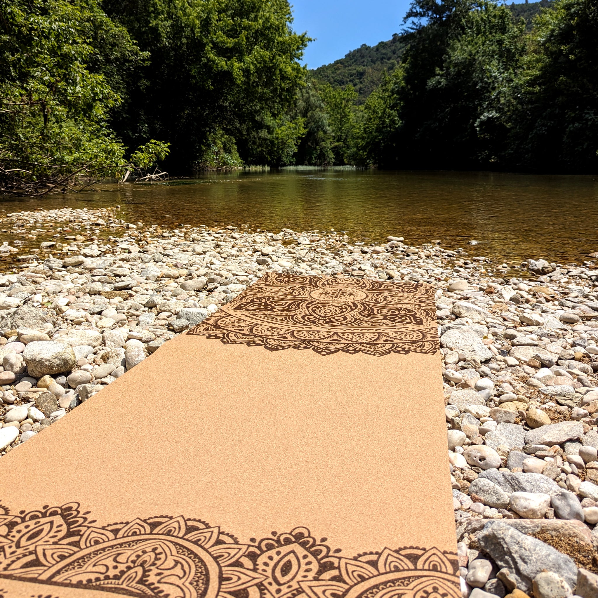Tapis de yoga en liège Cosmic Dance Mandala de ZenMotion posé sur la berge d'une rivière. Ce tapis écologique, orné d'un mandala vibrant, incarne énergie, équilibre et connexion à la nature. Conçu pour une pratique fluide et mindful, il offre une adhérence naturelle, une surface antibactérienne et un design inspirant. Idéal pour le Hatha, Vinyasa et la méditation, il célèbre l'harmonie et la transformation. Un compagnon parfait pour une pratique yoga en pleine nature.