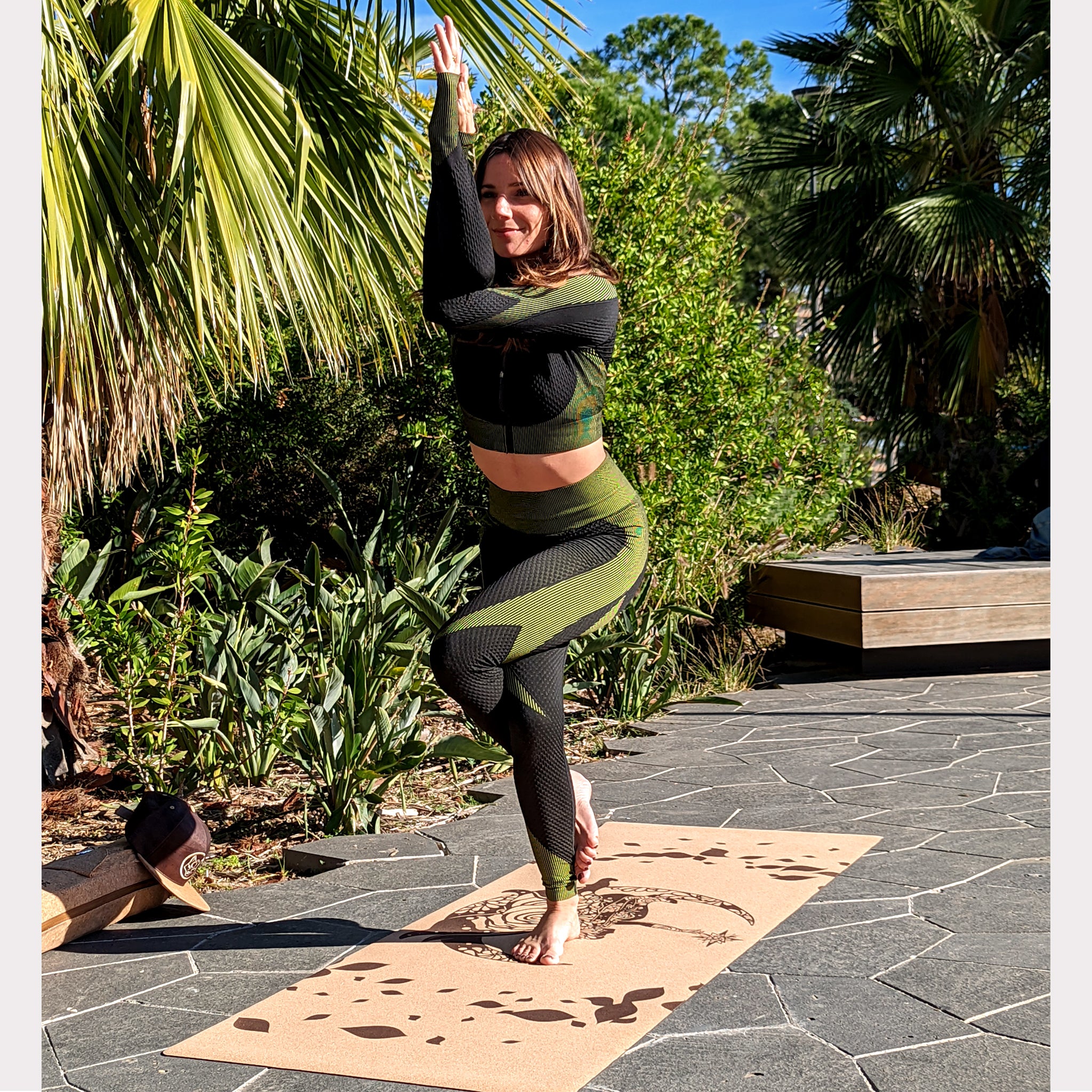 Belle femme faisant la posture de garudasana sur le tapis de yoga en liège Fairy Tale de ZenMotion. Plongez dans un univers enchanté le tapis est capturé ici dans un champ bucolique sous un mimosa. Inspiré des fées, ce design délicat mêle motifs mandalas et une rose cachée, symbolisant légèreté, créativité et magie. Le liège naturel offre une adhérence ultime et un confort inégalé, parfait pour une pratique fluide de Hatha ou de Yin yoga. Éco-responsable et élégant, ce tapis transforme chaque séance.