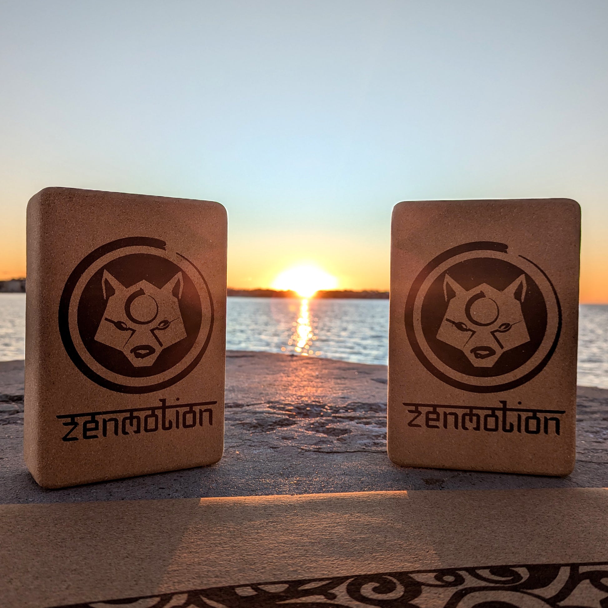 Deux briques de yoga ZenMotion posées sur un tapis en liège, avec un lever de soleil en bord de mer en arrière-plan. Accessoires écologiques et naturels, parfaits pour améliorer l'alignement, la souplesse et la stabilité lors de vos pratiques de Hatha, Vinyasa ou méditation. Une scène apaisante, symbolisant harmonie, énergie positive et connexion mindful avec la nature.