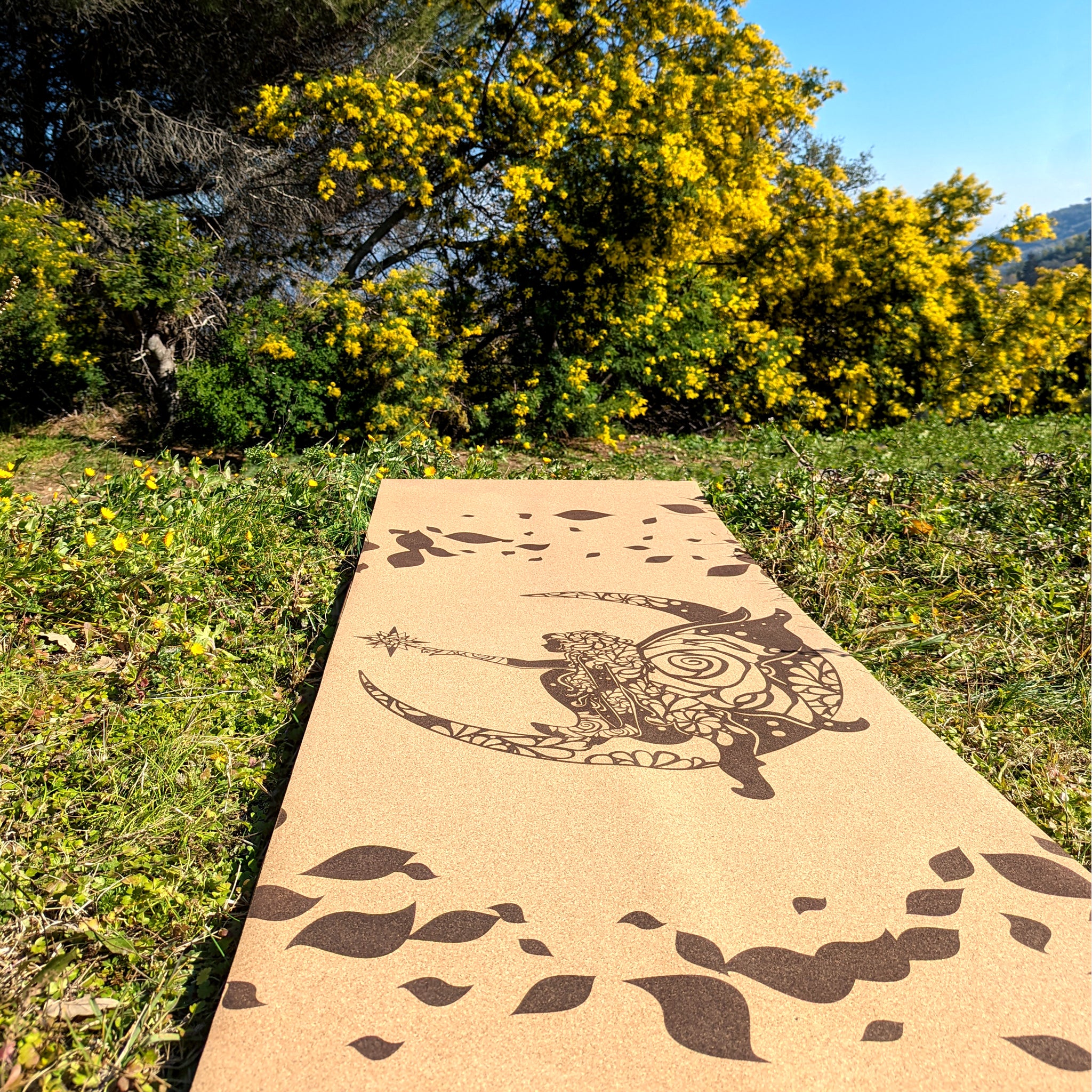 Tapis de yoga en liège Fairy Tale de ZenMotion. Plongez dans un univers enchanté le tapis est capturé ici dans un champ bucolique sous un mimosa. Inspiré des fées, ce design délicat mêle motifs mandalas et une rose cachée, symbolisant légèreté, créativité et magie. Le liège naturel offre une adhérence ultime et un confort inégalé, parfait pour une pratique fluide de Hatha ou de Yin yoga. Éco-responsable et élégant, ce tapis transforme chaque séance en une expérience spirituelle et imaginative.